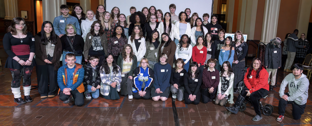 The image is of many of the emerging young artists whose work was included in the 2025 EYA award show and gallery exhibition. About 50 high school students are arranged in four rows. The photo was taken in the stage area at Landmark Center.